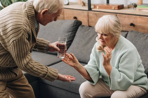 老婆を見て 薬と水のガラスを与える年配の男性 — ストック写真