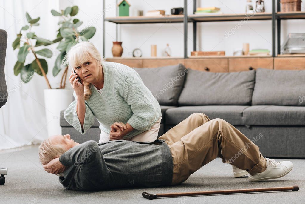 senior woman holding hand of dying old man with walking stick and looking at camera