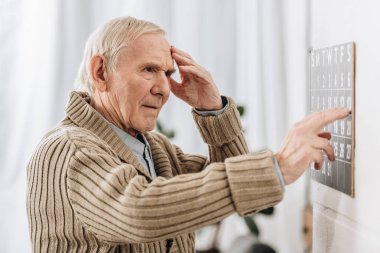 senior man looking at wall calendar and touching head clipart