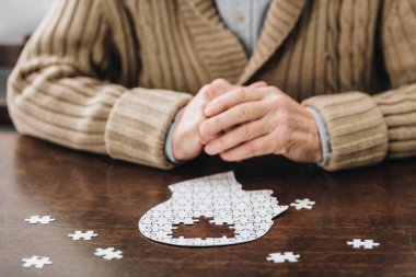 cropped view of senior man playing with puzzles on table clipart