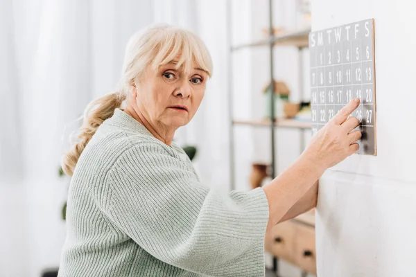 Upprörd Senior Kvinna Röra Väggkalender Och Tittar Kameran — Stockfoto