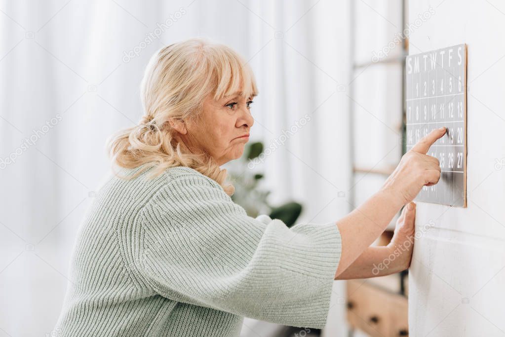 upset senior woman touching wall calendar and remembering dates