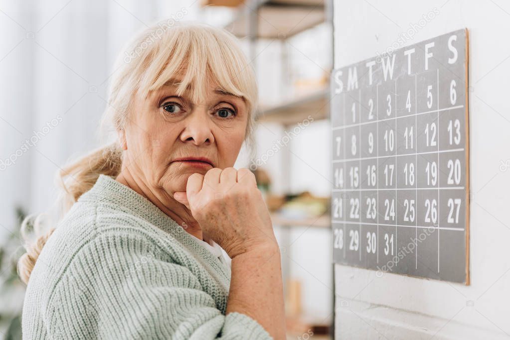 upset senior woman touching head and looking at camera