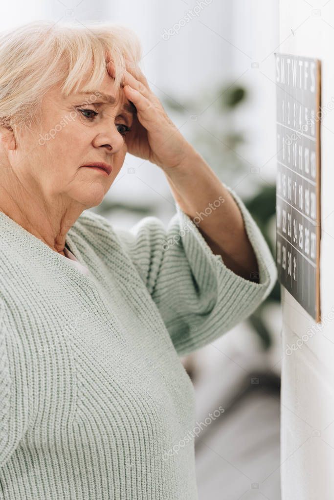 upset senior woman looking at calendar on wall 
