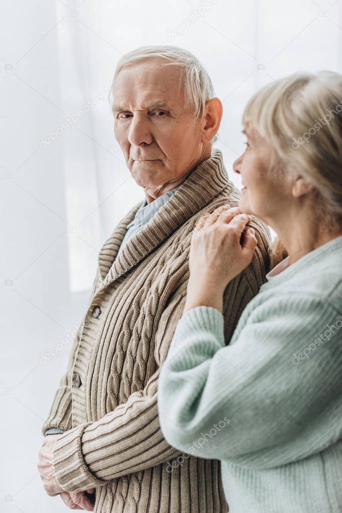 senior wife looking at retired husband and standing at home