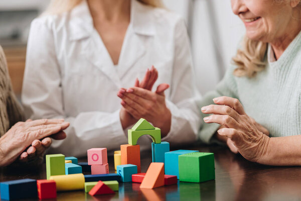 cropped view of caregiver applauding to retired couple while playing with wooden toys