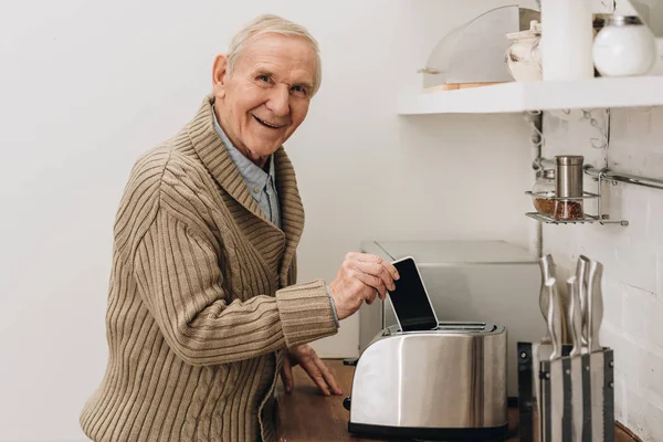 Happy Senior Man Dementia Disease Putting Smartphone Toaster — Stock Photo, Image