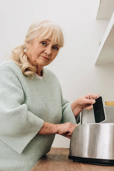 Senior Kobiety Chorobą Alzheimera Umieszczenie Smartfona Toster — Zdjęcie stockowe