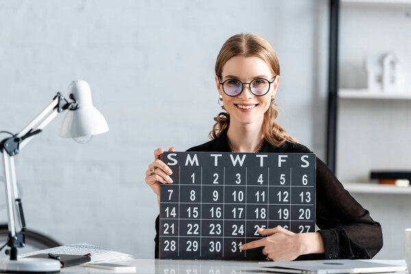 beautiful businesswoman in black clothes and glasses holding calendar and smiling at camera