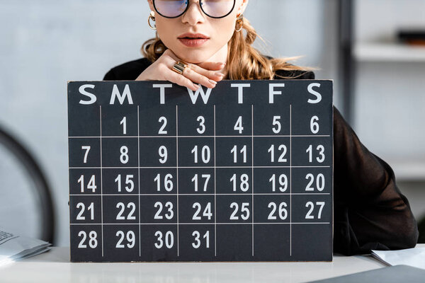 businesswoman in black clothes and glasses holding calendar 