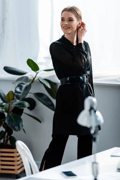 オフィスで髪に触れる黒い服を着た美しい笑みを浮かべて実業家 — ストック写真