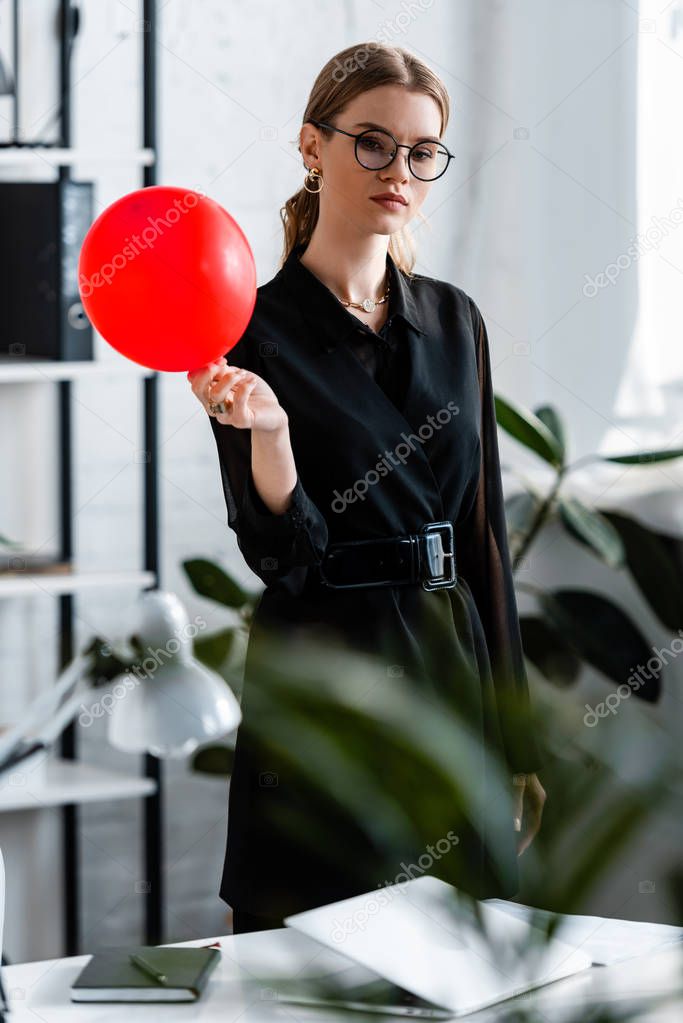 attractive woman in black clothes holding red balloon and looking at camera