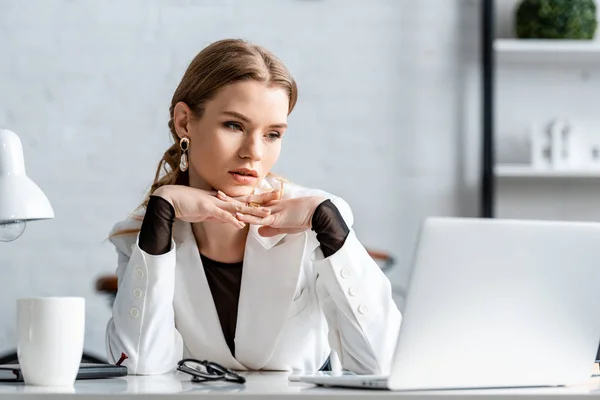 職場でコンピューターの机に座って手を組んで白のフォーマルな服装の女性実業家 — ストック写真