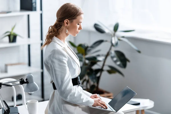 集中的女商人在白色正式服装坐在办公桌上 并在工作场所使用笔记本电脑 — 图库照片