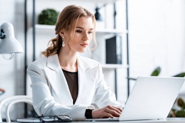 masada oturan ve işyeri dizüstü bilgisayarda yazarak formal giyim içinde ciddi iş kadını