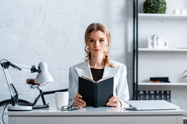 Concentrated Businesswoman Sitting Desk Holding Notebook Looking Camera Workplace — Stock Photo, Image