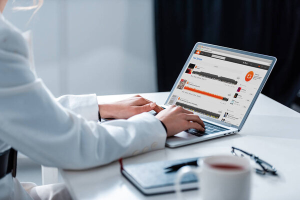 cropped view of woman using laptop with soundcloud website on screen at office desk