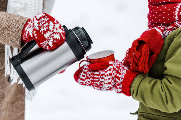 cropped view of mother pouring tea from thermos in red cup holding by child on white background