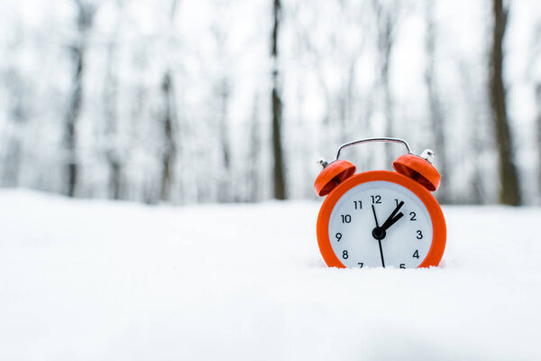 red retro clock standing on white snow near trees in snowy forest