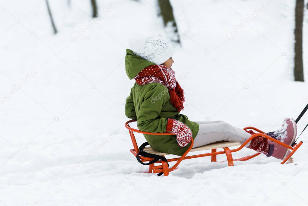 cute african american child riding on sleigh in park in snowy forest