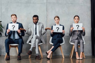 multiethnic businesspeople holding cards with question marks in waiting hall clipart