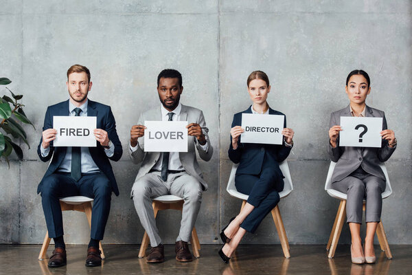 multiethnic businesspeople holding cards with 'lover', 'director', 'fired' words and question mark in waiting hall