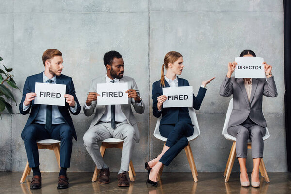 multiethnic businesspeople holding cards with 'fired' and 'director' words in waiting hall