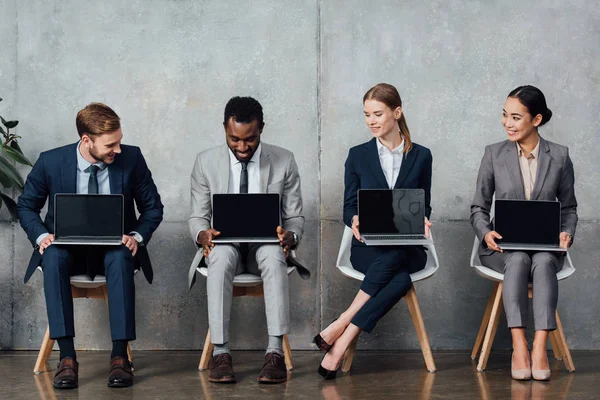 Empresários Multiétnicos Sorridentes Sentados Cadeiras Segurando Laptops Com Tela Branco — Fotografia de Stock
