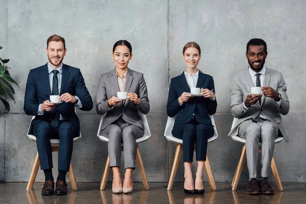 Empresarios Multiétnicos Sentados Sillas Tomando Café Mirando Cámara Sala Espera — Foto de Stock