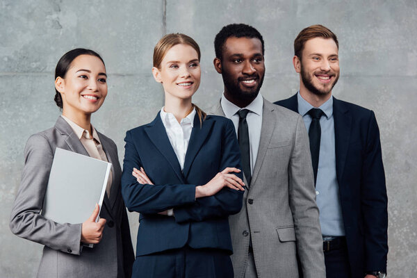 smiling multiethnic group of businesspeople in formal wear posing and looking away