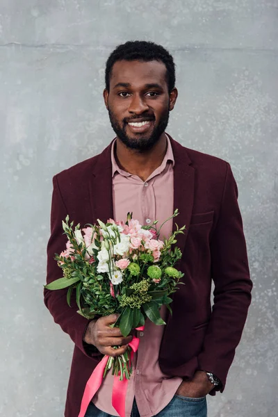 非洲裔美国人穿着休闲装 拿着鲜花 看着灰色背景的相机 — 图库照片