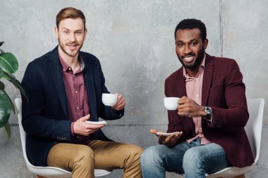 oturan, bekleme salonunda kahve içme ve kameraya bakarak çok ırklı yakışıklı erkekler