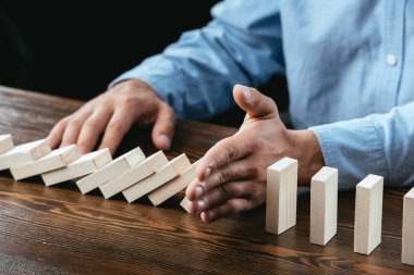 partial view of man sitting at desk and preventing wooden blocks from falling  clipart