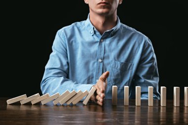 cropped view of man sitting at desk and preventing wooden blocks from falling  clipart
