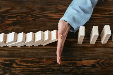 close up view of woman at desk and preventing wooden blocks from falling with hand clipart