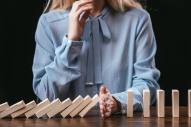 cropped view of woman in blue blouse sitting at desk and preventing wooden blocks from falling with hand
