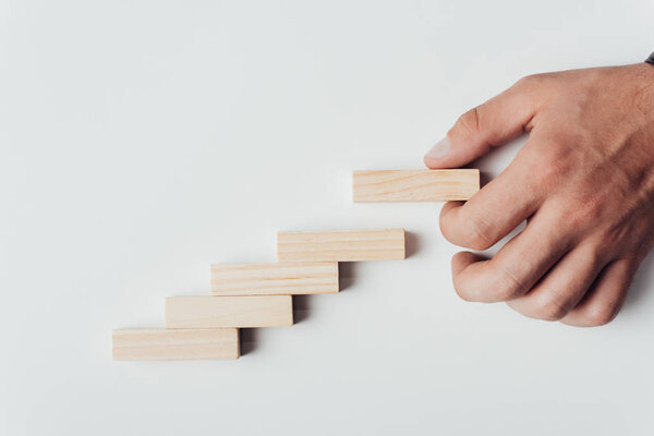 cropped view of man putting wooden brick on top of wooden blocks symbolizing career ladder isolated on white