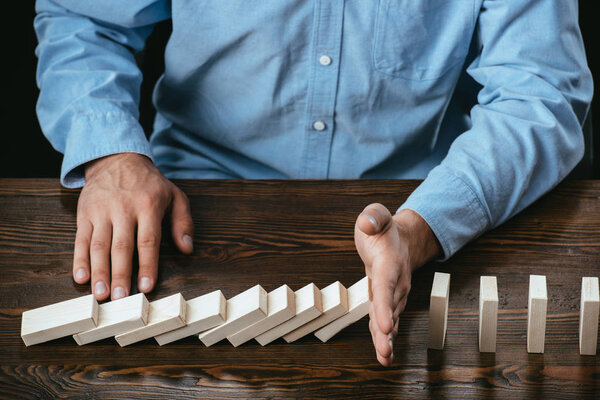 partial view of man sitting at desk and preventing wooden blocks from falling 