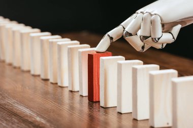 selective focus of robotic hand picking red wooden brick from row of blocks on desk clipart