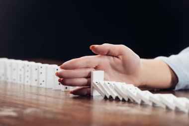 cropped view of woman preventing dominoes from falling on desk isolated on black clipart
