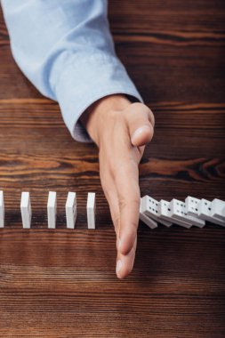 top view of man preventing dominoes from falling on wooden desk clipart