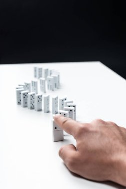 cropped view of man pointing at domino row on white table isolated on black clipart