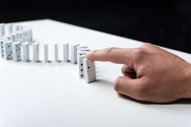 partial view of man pointing at domino row on white table isolated on black clipart