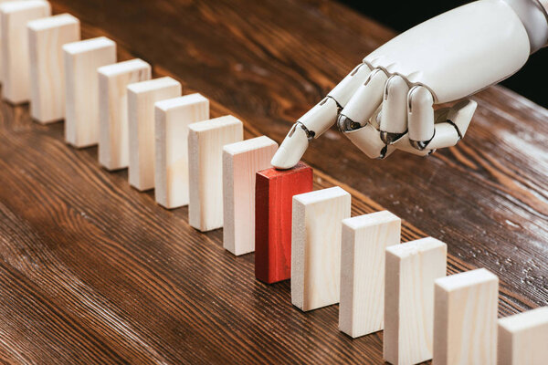 selective focus of robotic hand picking red wooden brick from row of blocks on desk