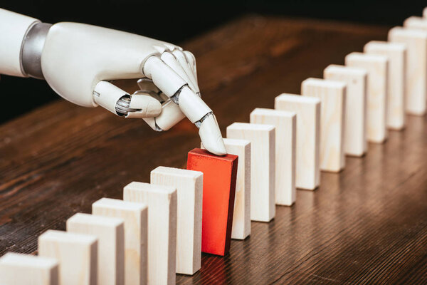 robotic hand picking red wooden brick from row of blocks on desk