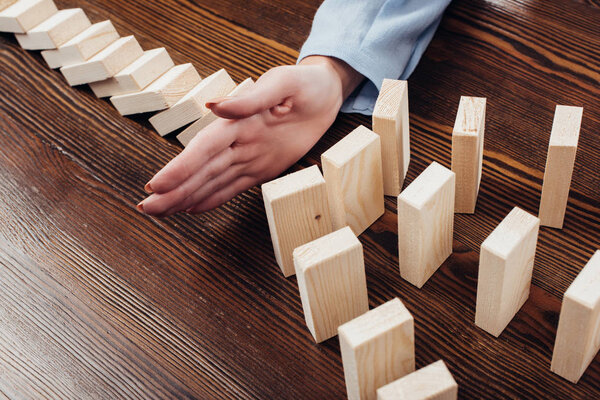 partial view of woman preventing wooden blocks from falling at desk