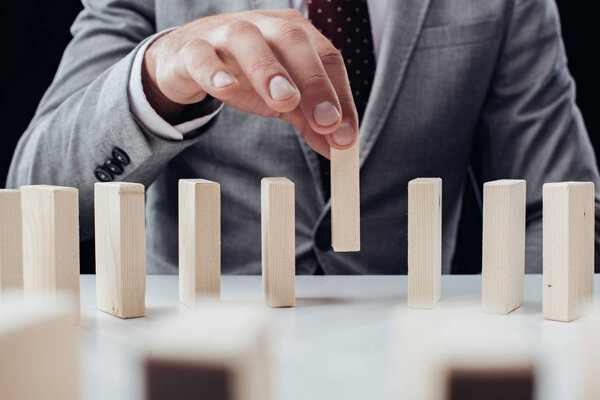 close up view of man picking wooden brick from row of blocks on desk