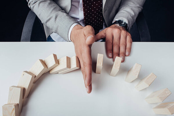 partial view of businessman preventing wooden blocks from falling