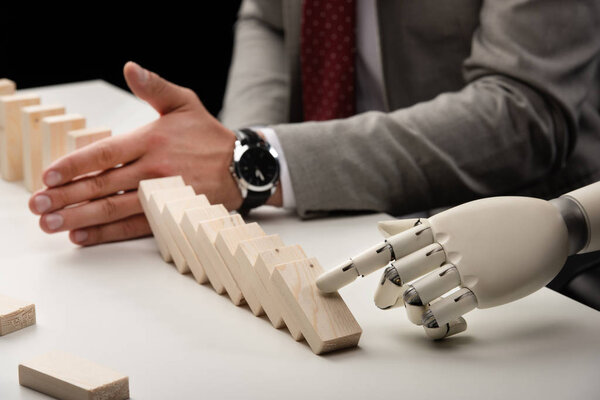 cropped view of robotic hand pushing wooden bricks while man preventing row from falling