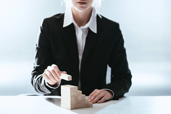 cropped view of woman putting wooden brick on top of wooden blocks symbolizing career ladder with backlit